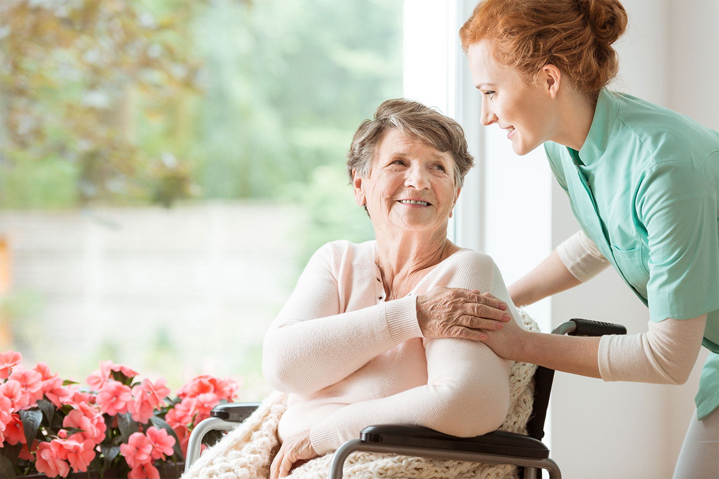 Ein Gesellschafter vom Pflegedienst Vitanova Hamburg lächelt eine älteren Dame im Rollstuhl zu